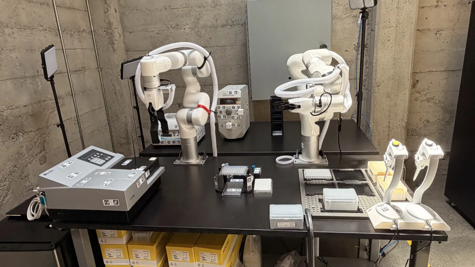 Two robotic arms on a lab bench with a plate reader, microplates, and pipettes during the TEM-1 screen