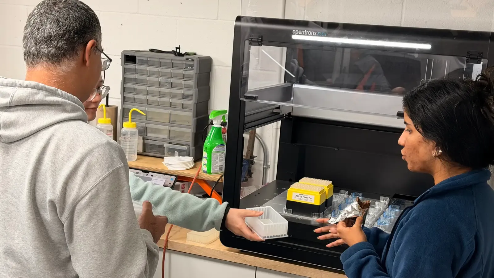 Two builders loading tip racks and labware onto the Opentrons Flex
